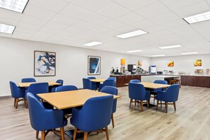 A spacious room with multiple tables and chairs, a kitchen area, and artwork on the walls.
