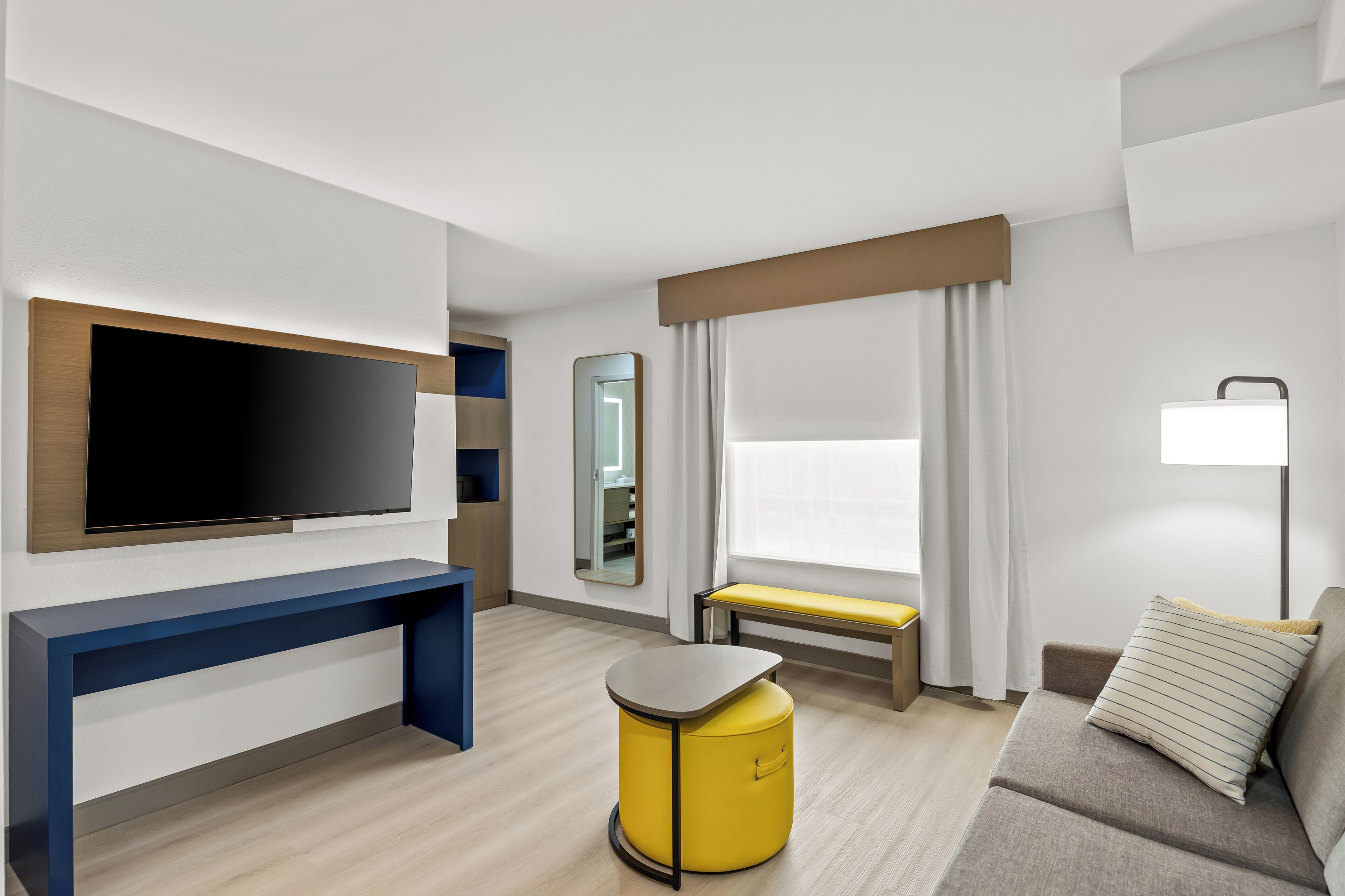 A modern hotel room with a flat-screen TV, a bench, a sofa, and a bedside table.