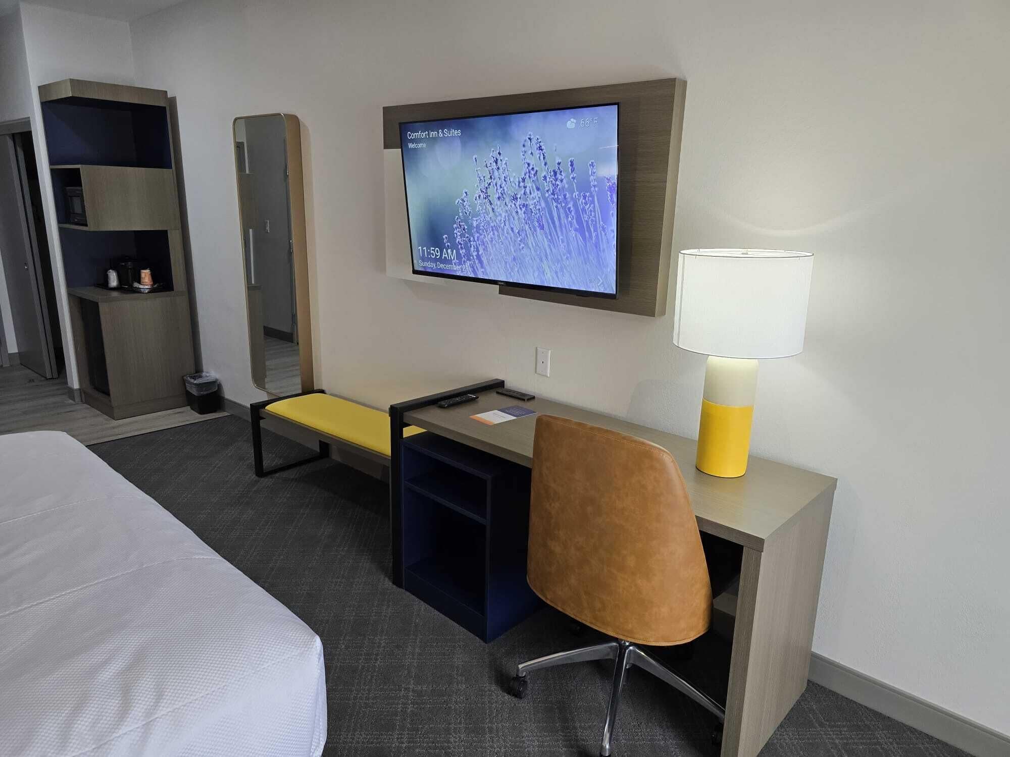 Une chambre d’hôtel comprenant un lit, un bureau avec une chaise, une télévision, une lampe et une armoire.