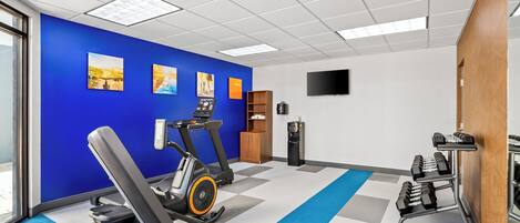 Un gimnasio con equipo de ejercicio, una pared azul y un ventanal grande.