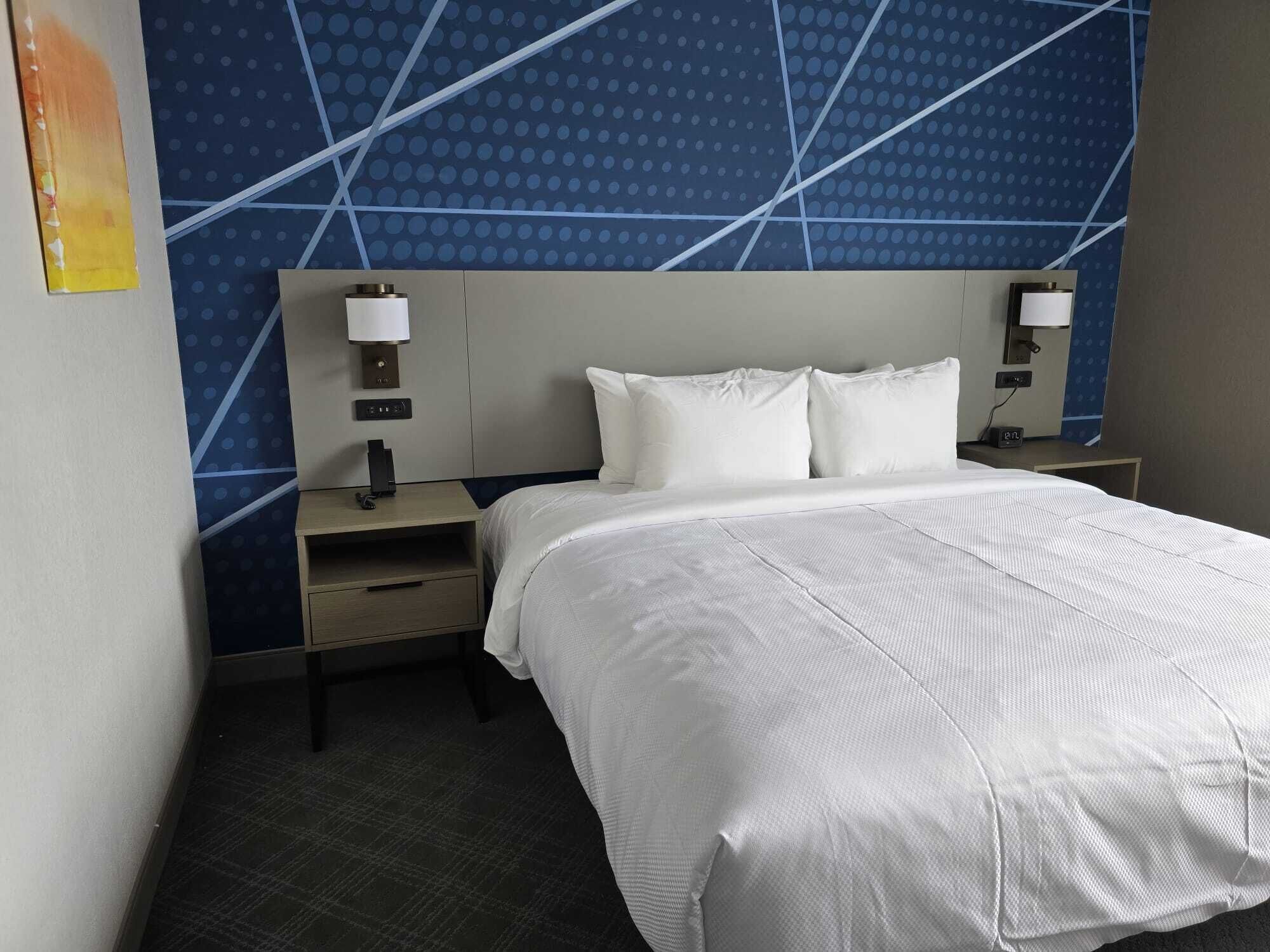 Une chambre d’hôtel avec un grand lit, deux tables de chevet, une tête de lit et un mur orné d’un motif à pois bleus.