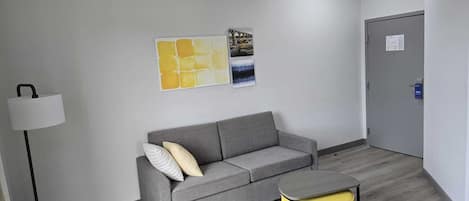 A modern, minimalistic room with a grey sofa, a yellow ottoman, and a floor lamp.