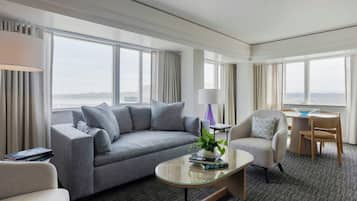 Una habitación de hotel moderna con sofá, sillón y una mesita con lámpara y planta.