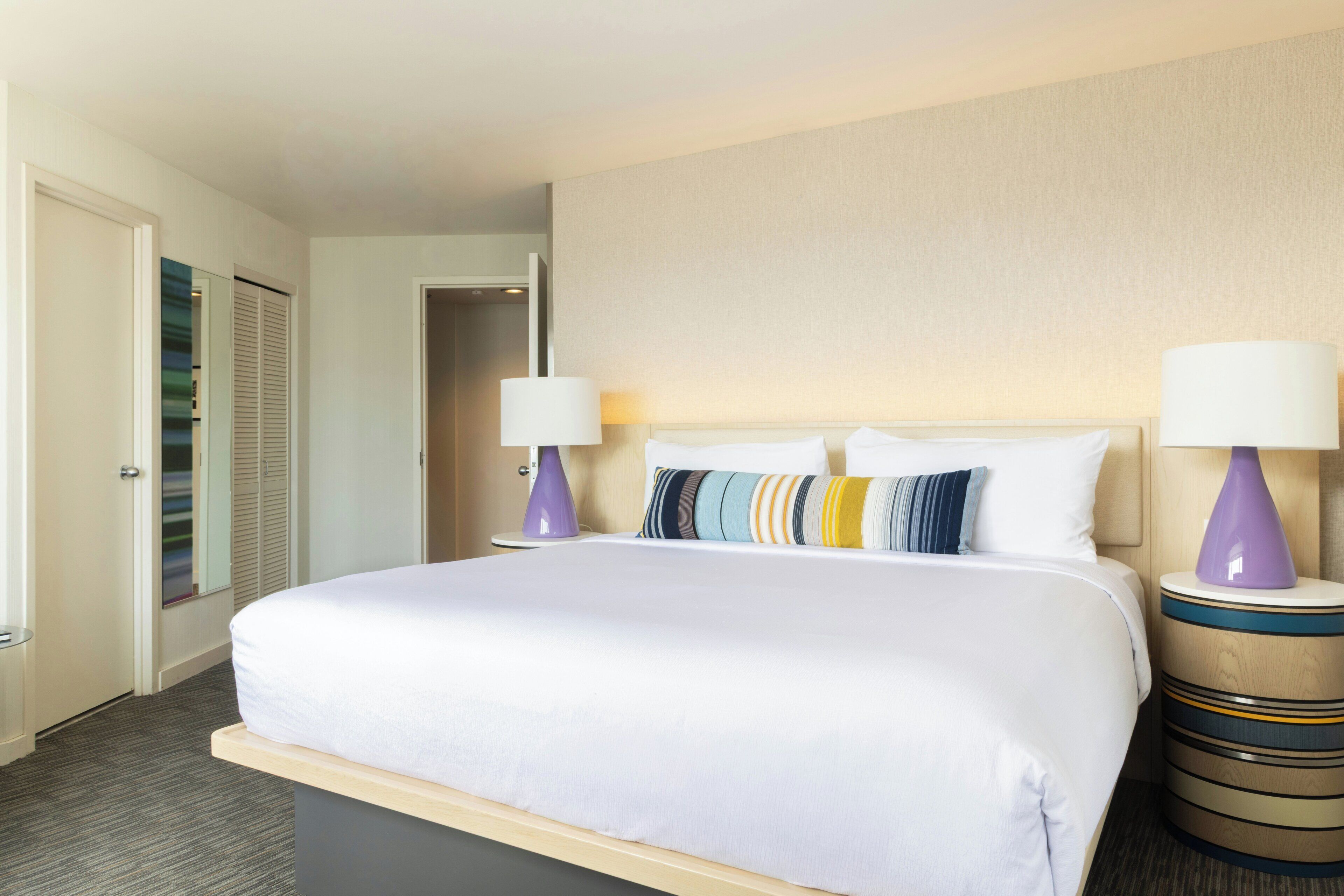 A hotel room with a large bed, two bedside lamps, a wooden headboard, and a closet with sliding doors.