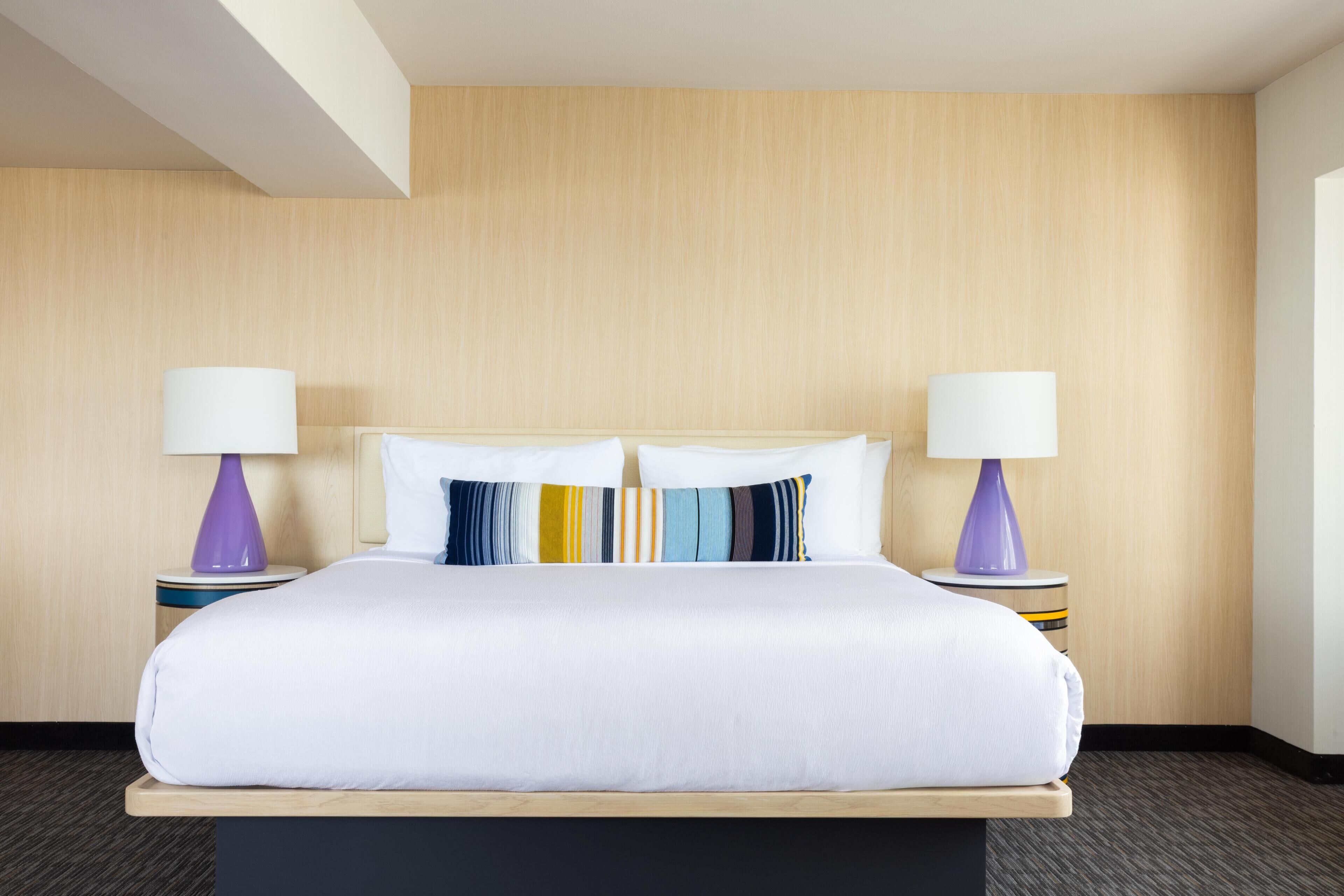 A hotel room with a large bed, two bedside lamps, and a wooden headboard.