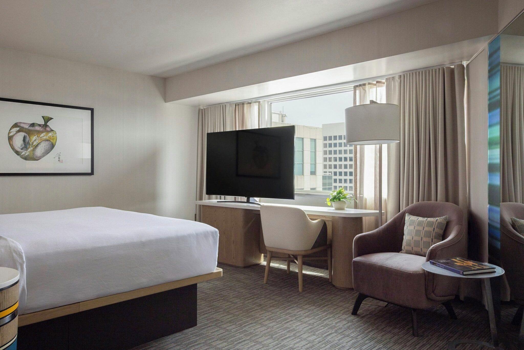 A hotel room with a bed, desk, TV, and seating area.