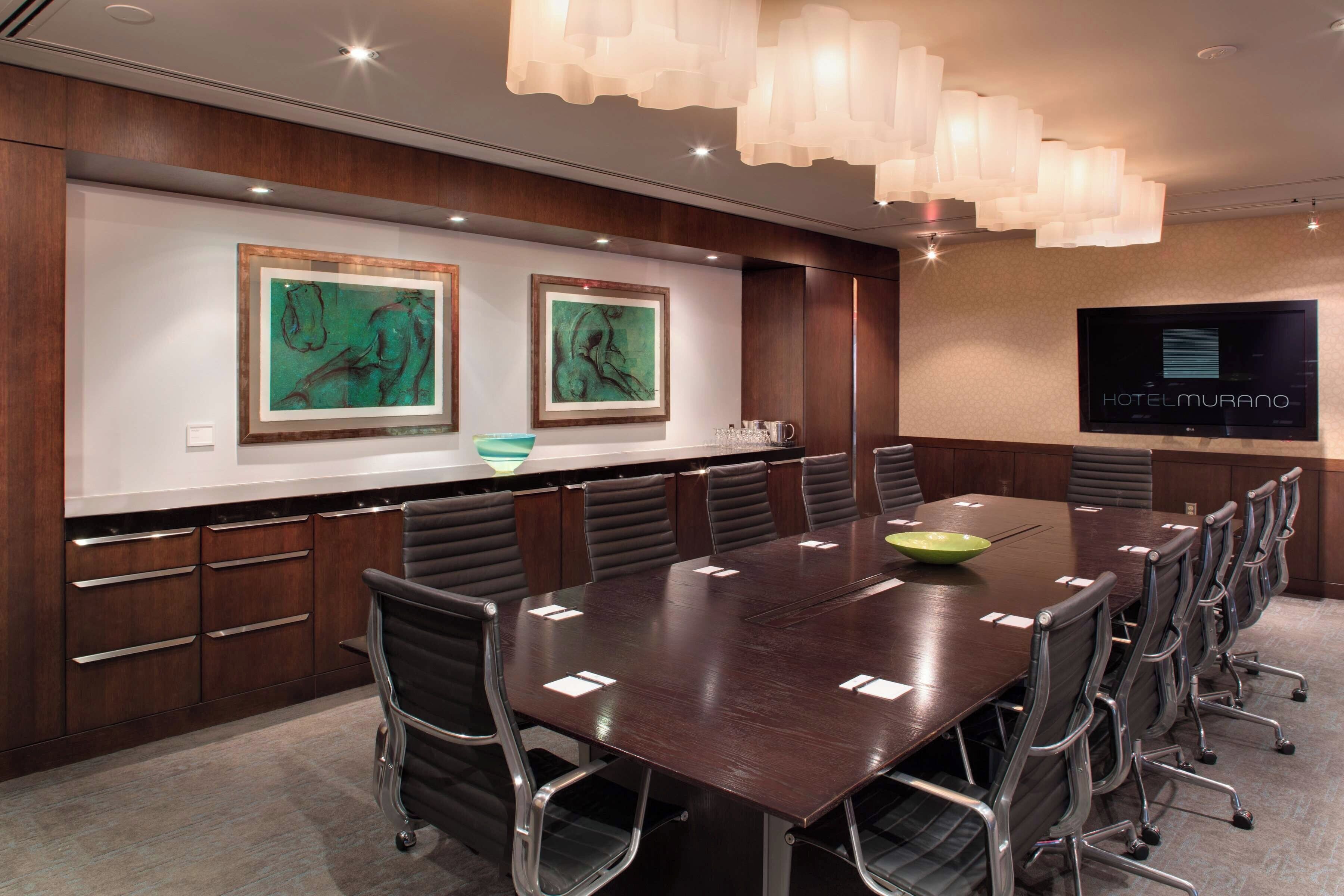 A conference room with a long table, chairs, a TV screen, and artwork on the walls.