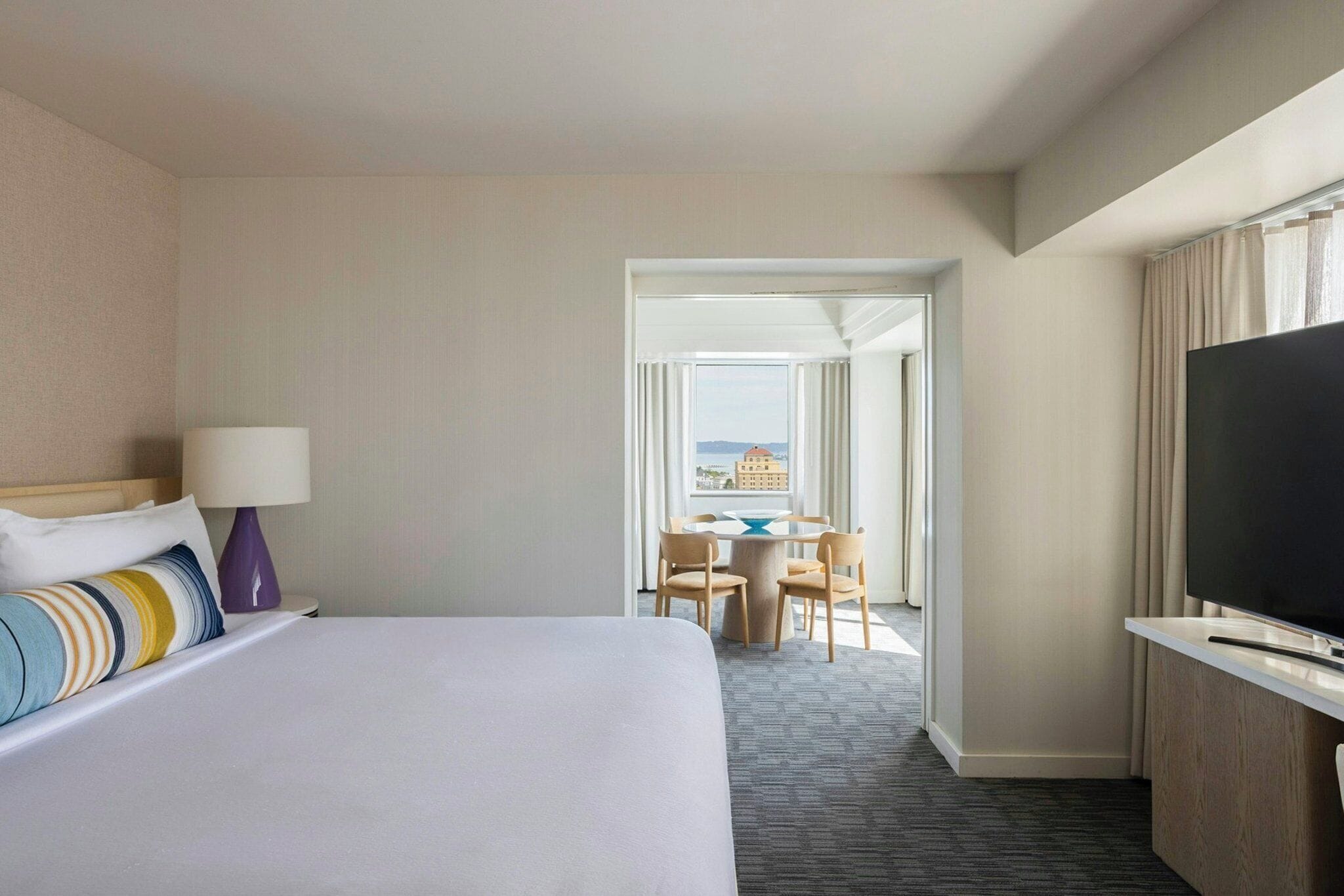 Ein Hotelzimmer mit Bett, Schreibtisch und Fernseher, mit Blick auf die Stadt durch das Fenster.