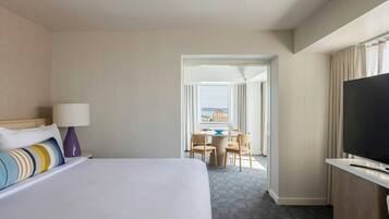 Habitación de hotel con cama, escritorio con televisor y vista a la ciudad a través del ventanal.