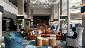 A spacious lobby with a leather sofa, blue armchairs, and a chandelier.