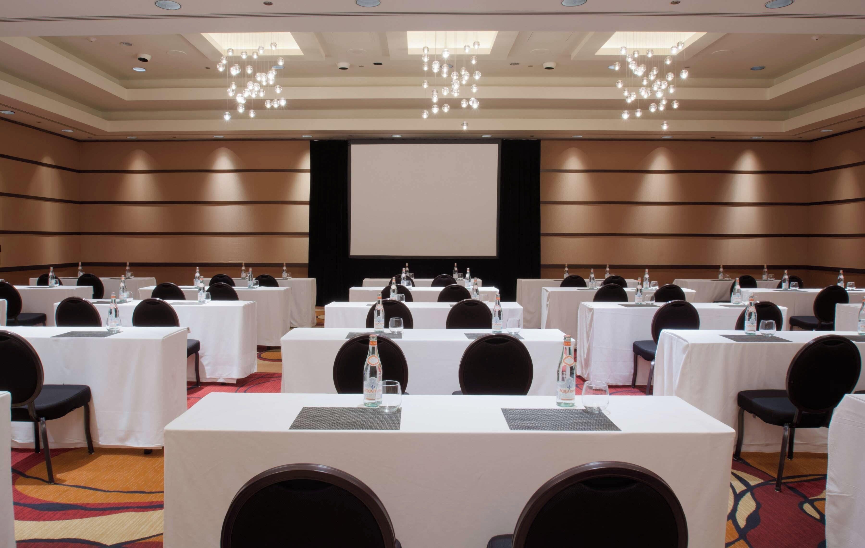 A conference room with multiple tables, chairs, and a large screen at the front.