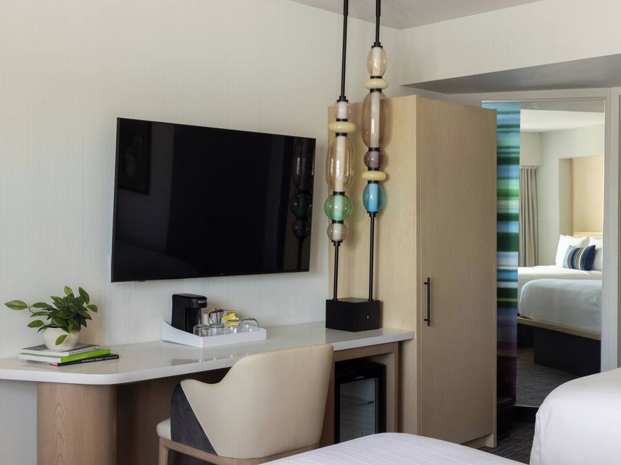 Ein Hotelzimmer mit Flachbildfernseher, Schreibtisch mit Kaffeemaschine, Stuhl, Kleiderschrank und Bett.