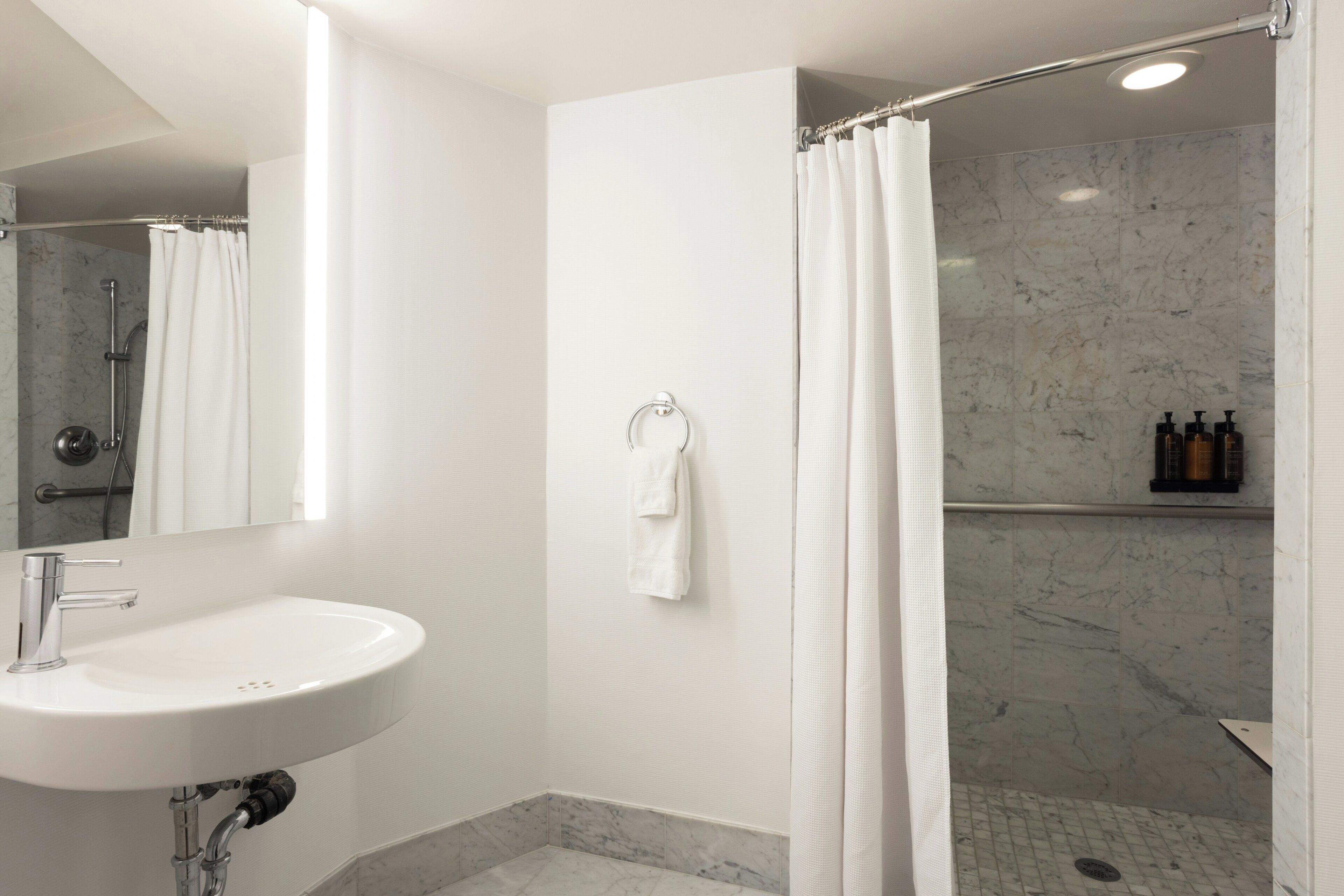 A modern bathroom with a white sink, a shower with a curtain, and a marble-tiled shower area.