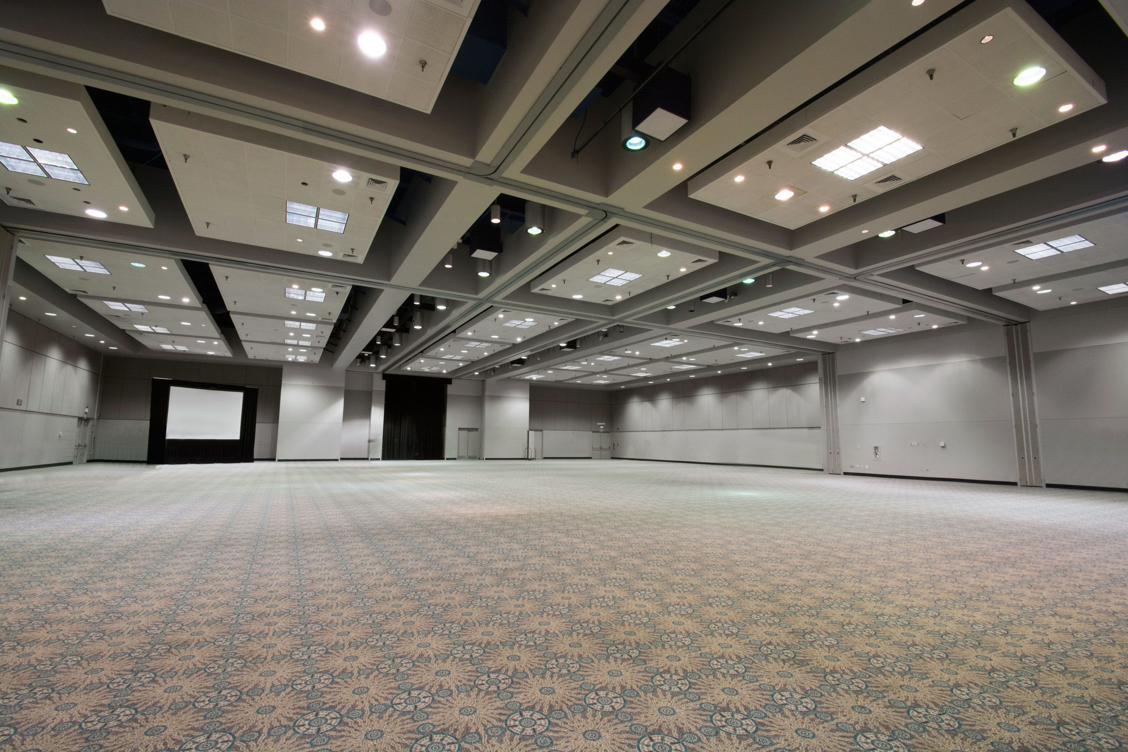 A large, empty conference room with patterned carpet, recessed lighting, and a projection screen.