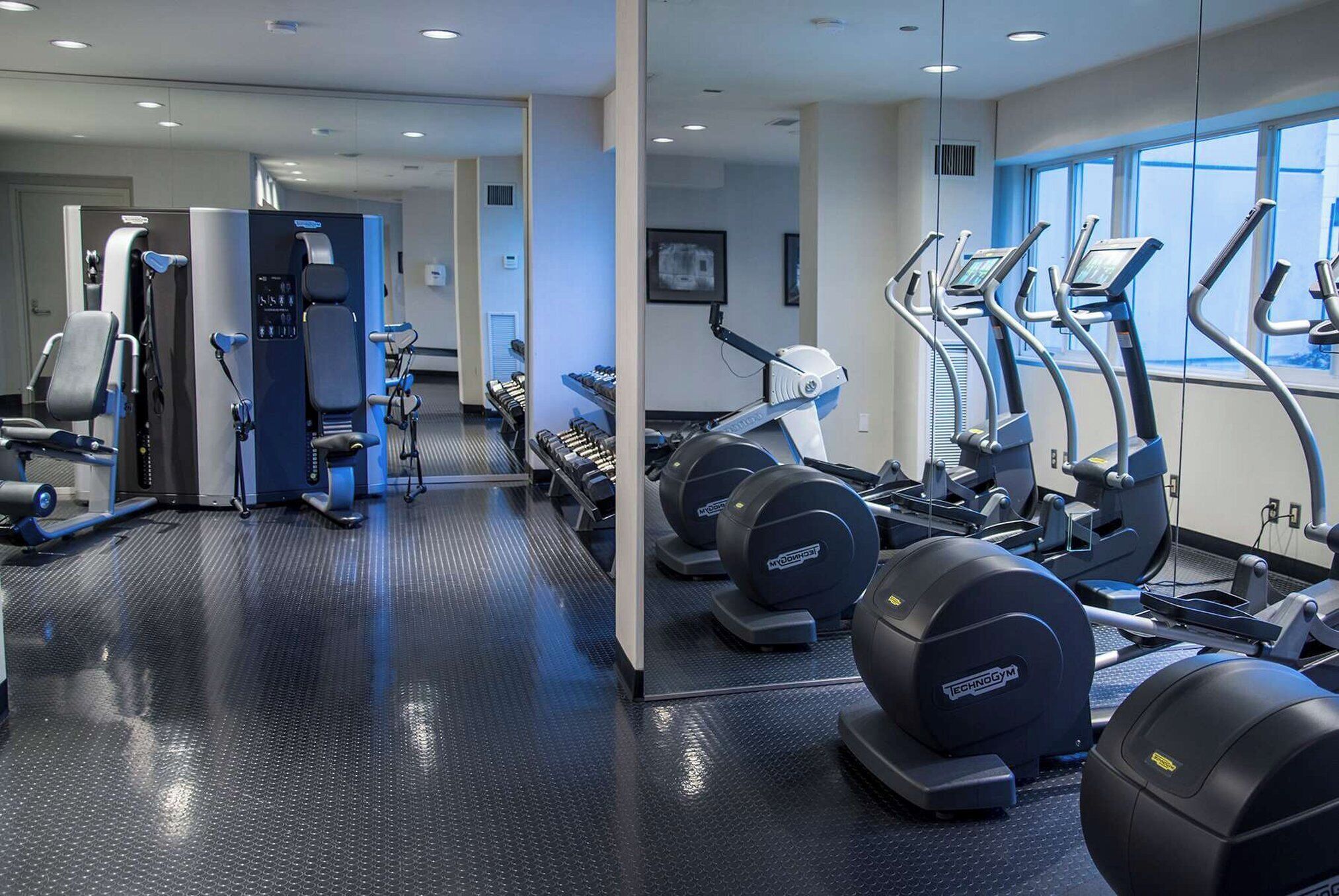 Un gimnasio con máquinas de cardio, pesas y un espejo grande.