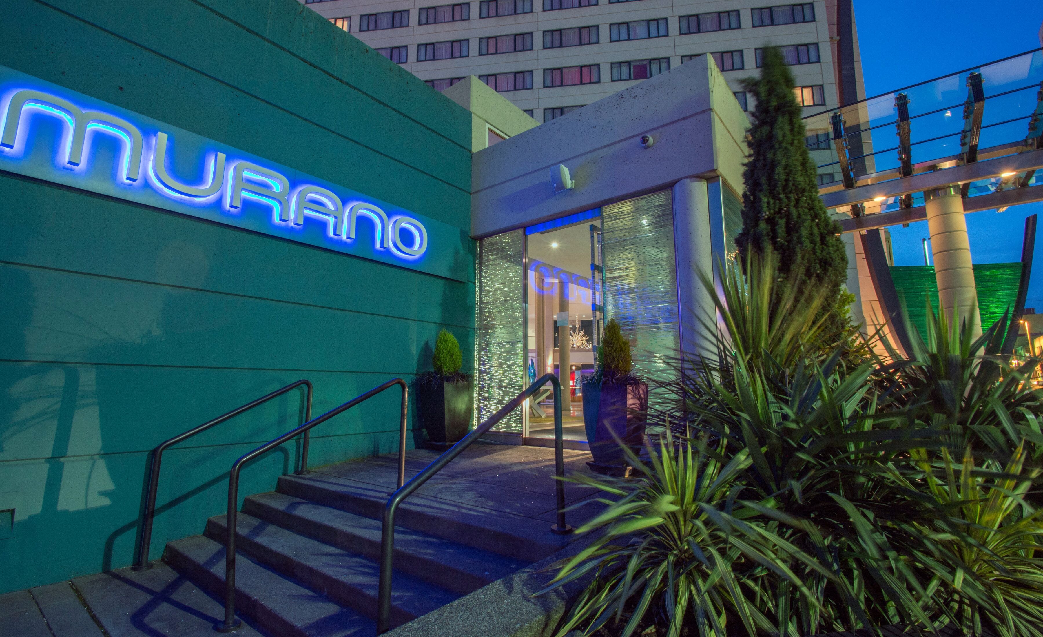 A hotel entrance with a neon sign, a staircase, and a glass facade.