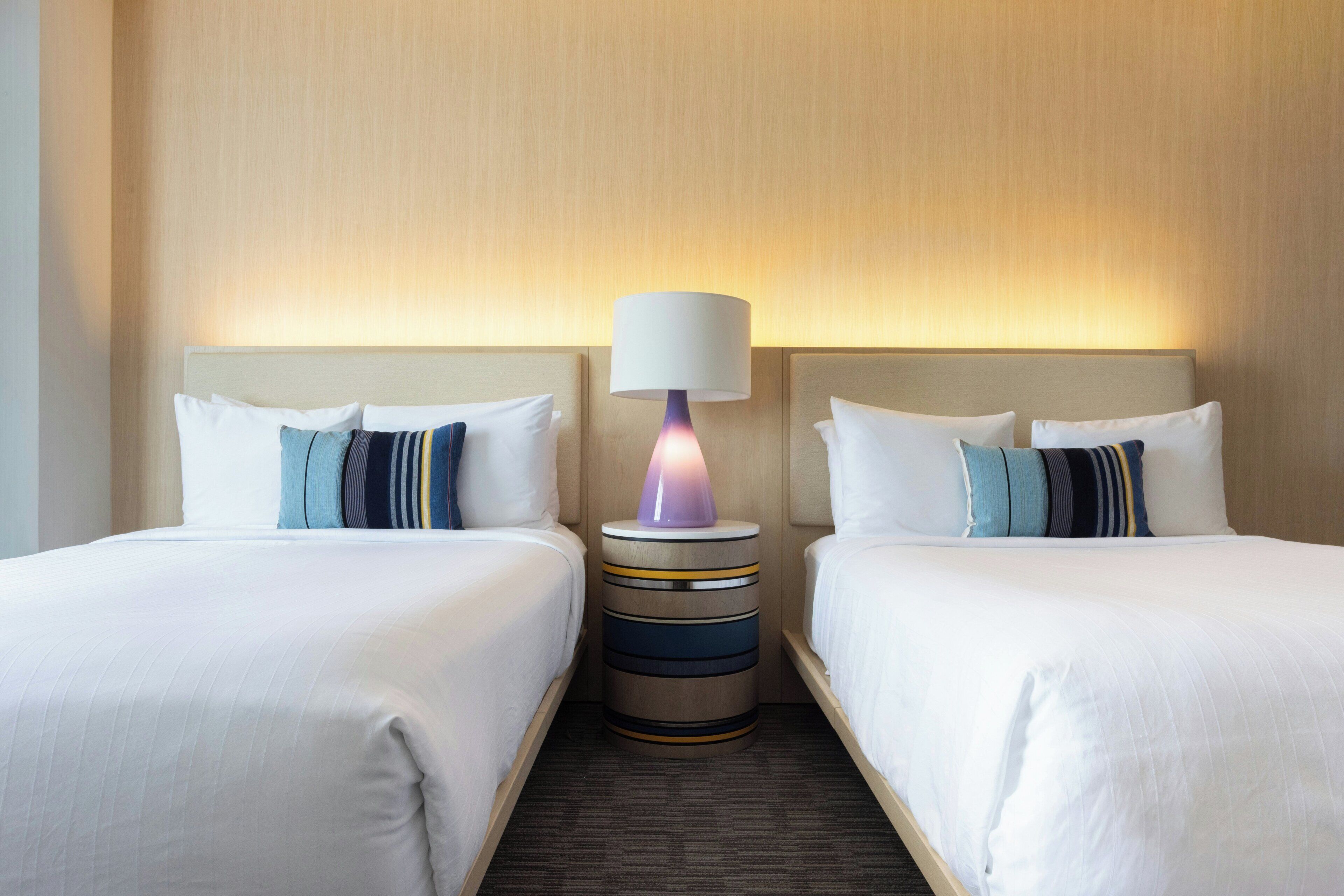 Ein Hotelzimmer mit zwei Betten, einem Nachttisch mit Lampe und Teppichboden.