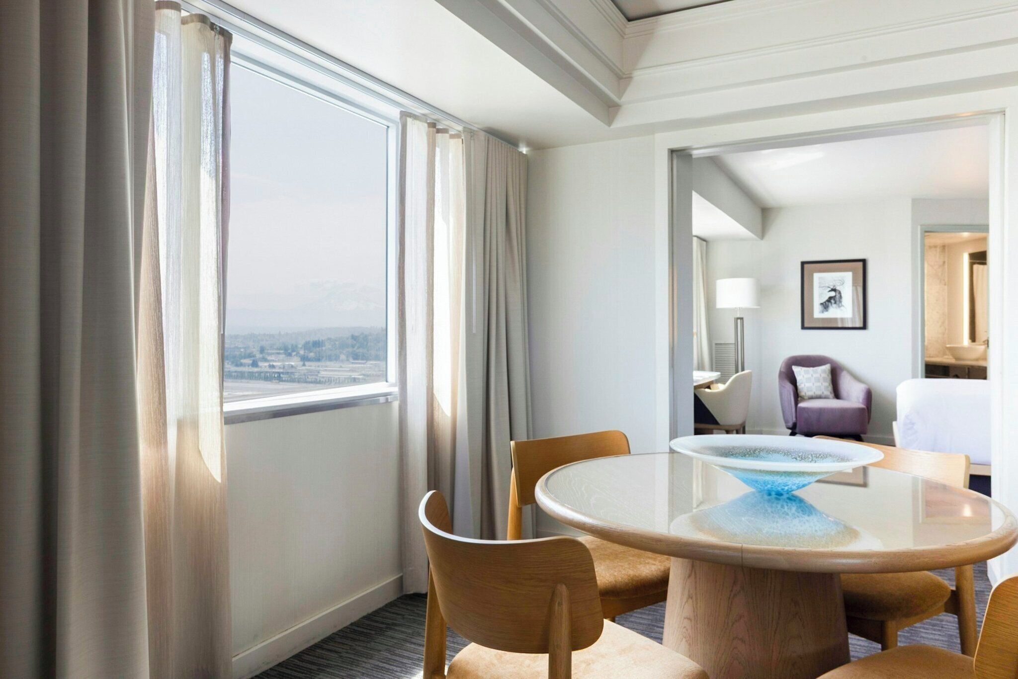 Habitación de hotel con comedor, vista por la ventana y baño visible a través de una puerta abierta.