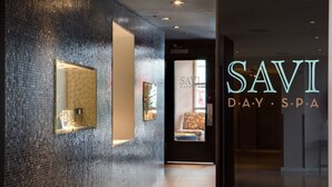 A modern spa interior with a dark tiled wall, a reception desk, and a visible spa area with a chair and a mirror.