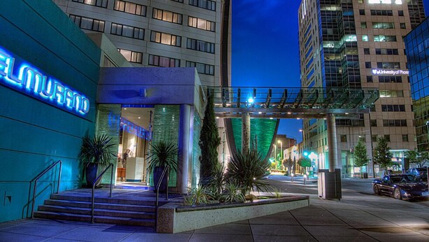 A modern hotel entrance with a neon sign, a covered walkway, and a parking area.