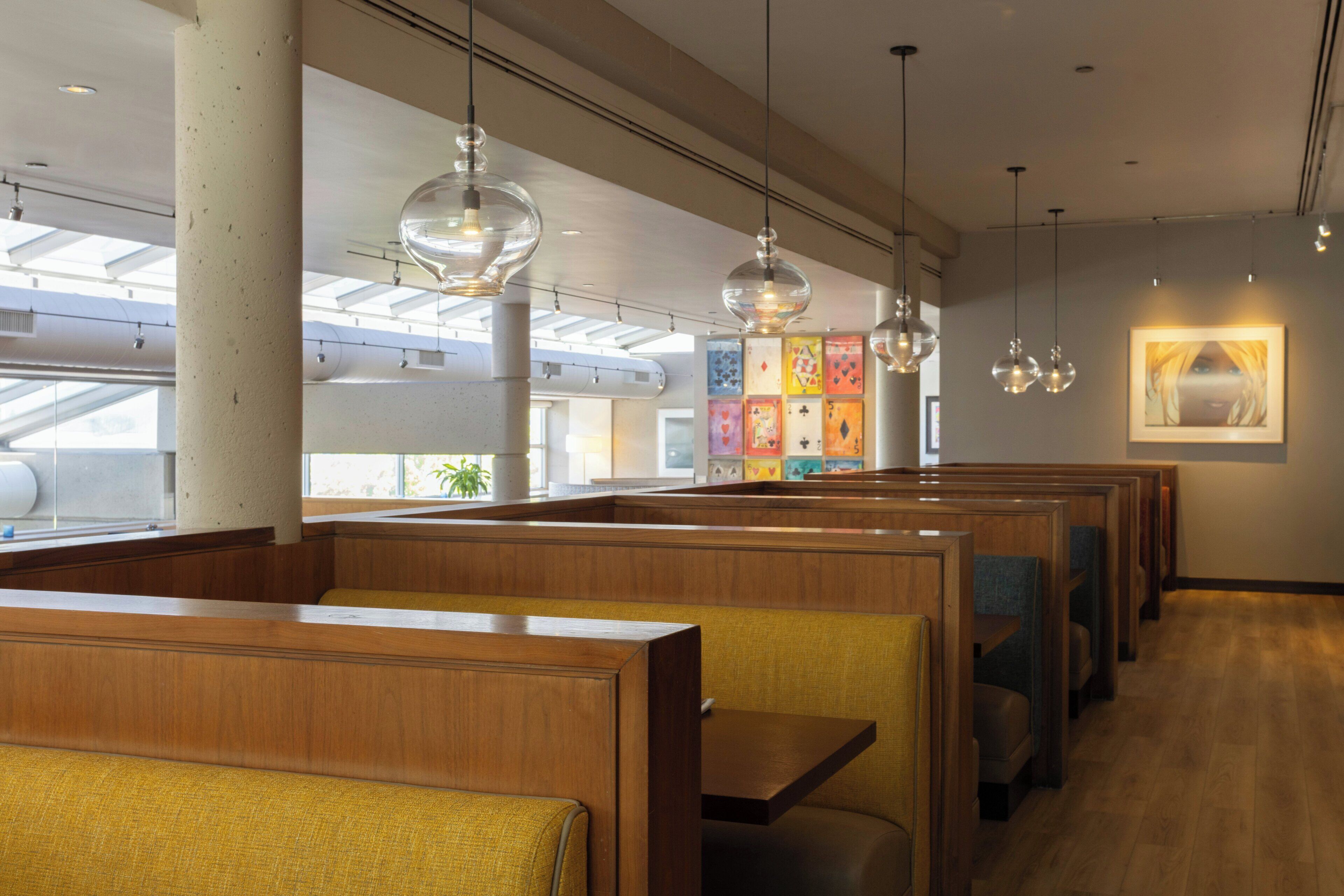 Un restaurant avec des banquettes en bois, des luminaires suspendus et un mur décoré d’œuvres d’art colorées.