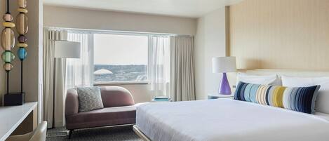 A hotel room with a bed, a sofa, a desk, and a view of the cityscape.