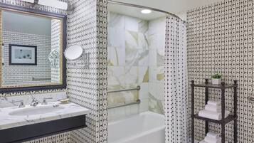 Un baño con lavamanos de mármol, bañera con puerta de vidrio y estante con toallas.