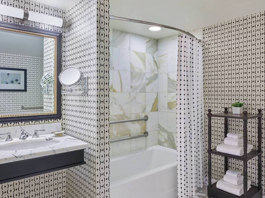 Un baño con lavamanos de mármol, bañera con puerta de vidrio y estante con toallas.