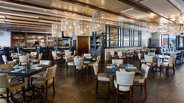 A spacious restaurant with multiple tables and chairs, a bar area, and large windows providing natural light. - The Alexandrian Old Town Alexandria, Autograph Collection (Alexandria)