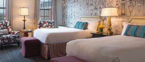 A hotel room with two beds, a chair, a lamp, and a patterned wall.