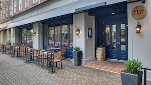A brick building with a covered outdoor seating area, wooden tables, and chairs. - The Alexandrian Old Town Alexandria, Autograph Collection (Alexandria)