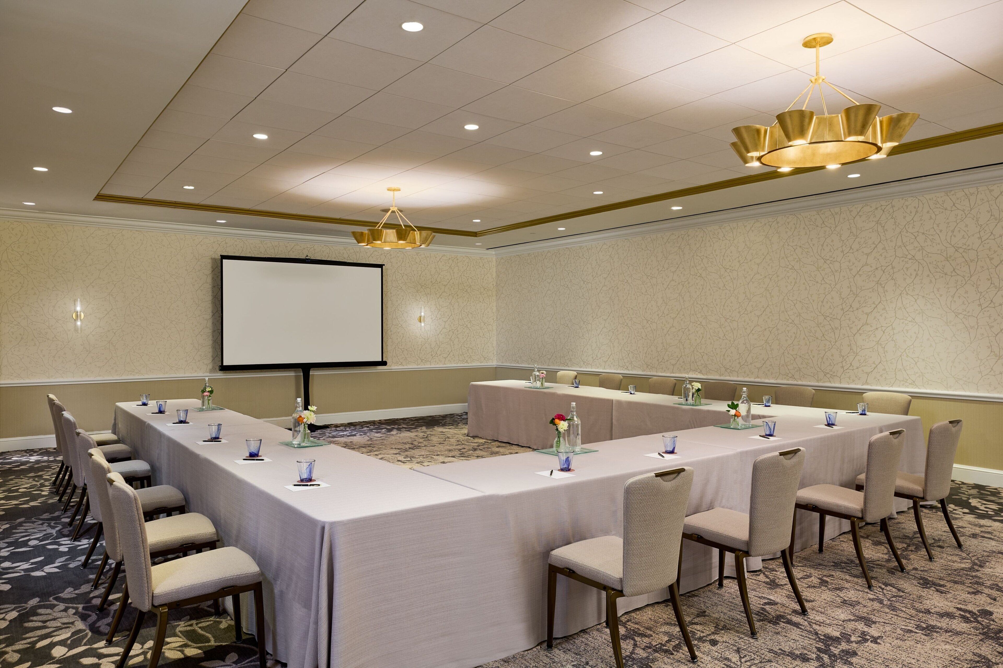 A conference room with a long table, chairs, a projector screen, and a chandelier.