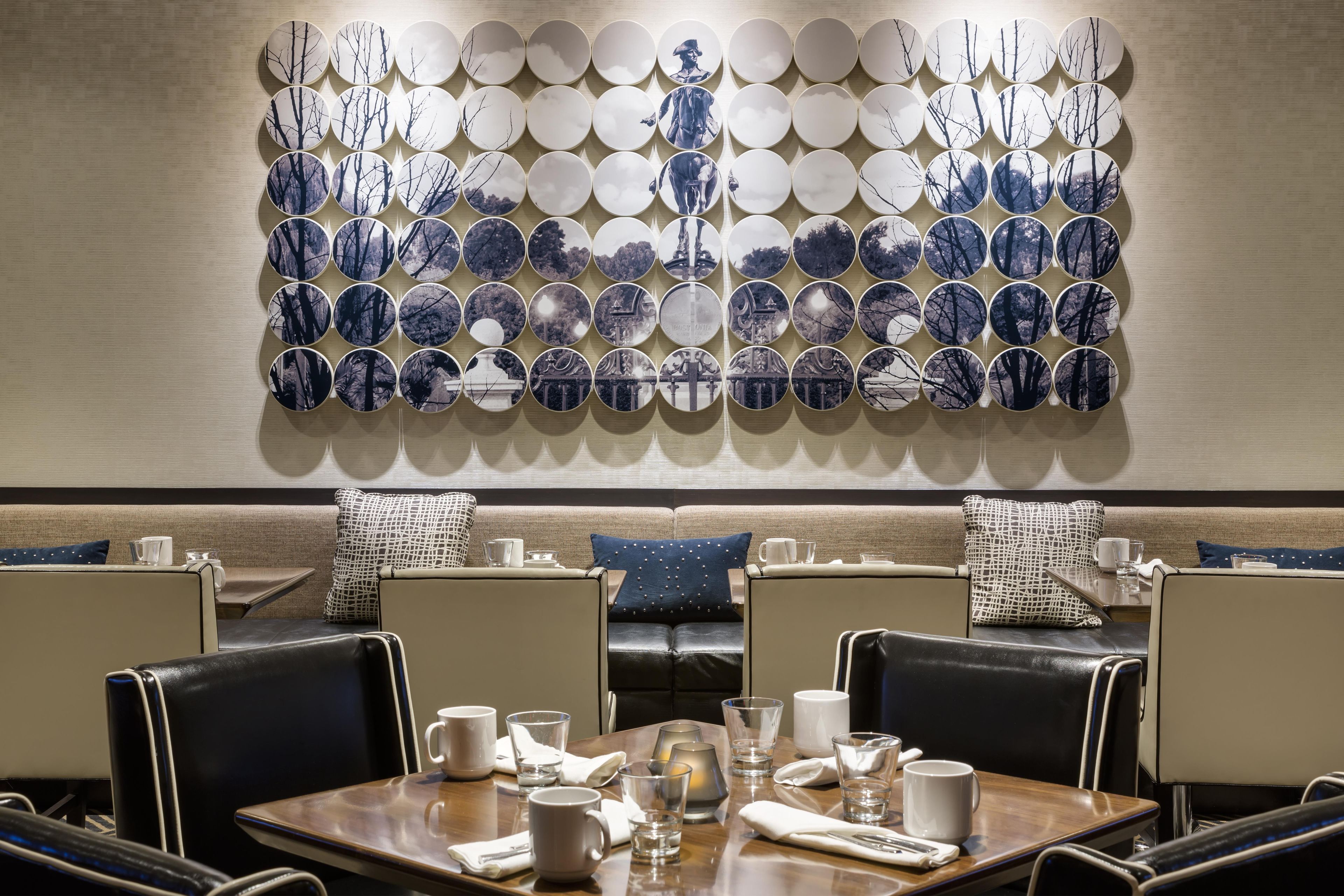 A dining area with a wall of circular photographs, a sofa with patterned cushions, and a table set for two.
