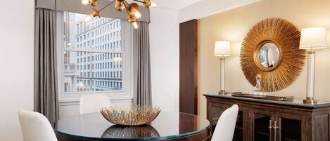 Een moderne hotelkamer met een ronde glazen tafel, twee witte stoelen, een decoratieve spiegel en een kroonluchter.