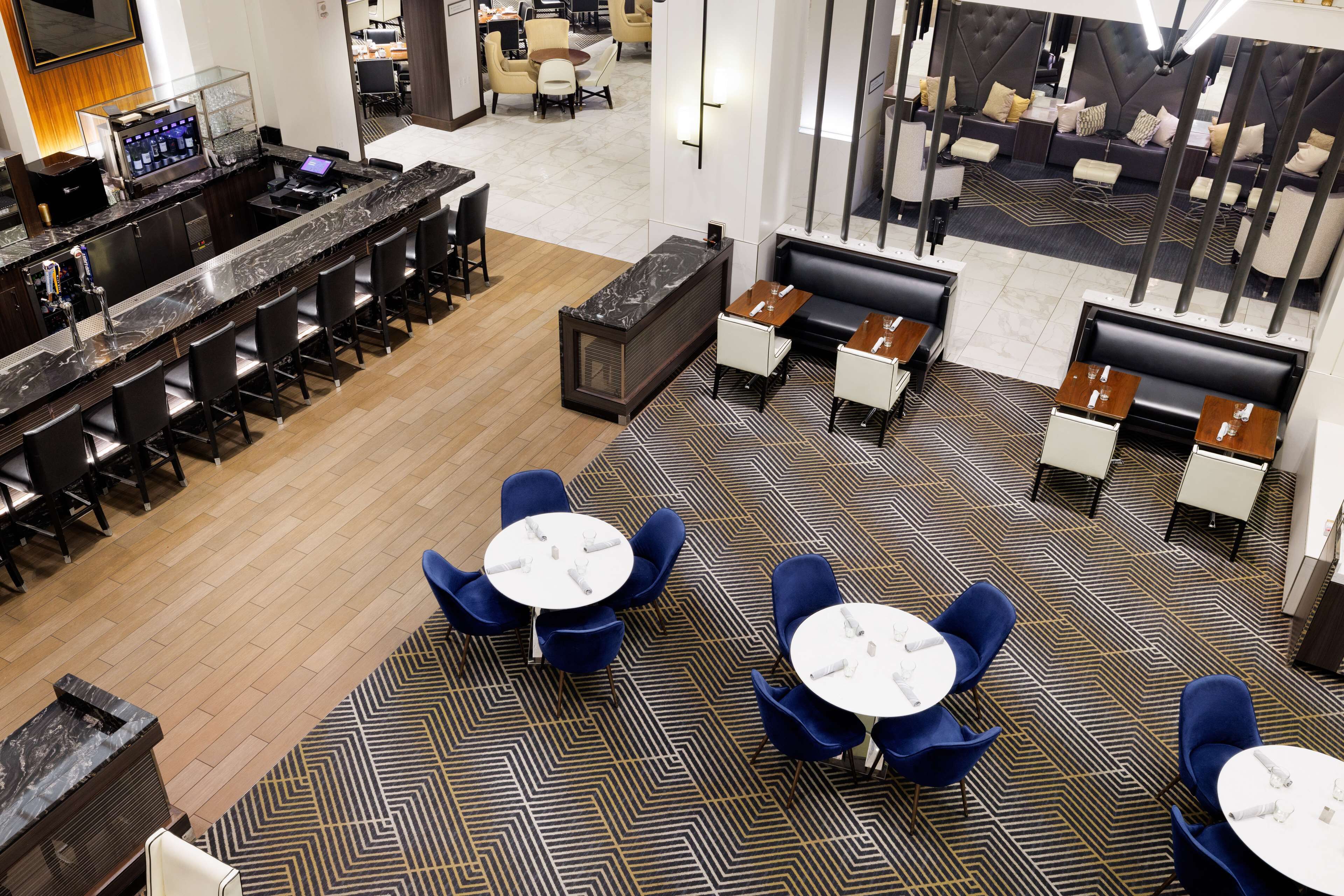 Um lobby de hotel moderno com uma recepção de mármore, várias áreas de estar e um carpete estampado.