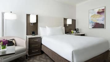 A hotel room with a large bed, a desk with a lamp, a chair, and a wall-mounted artwork.