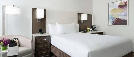 Une chambre d’hôtel avec un grand lit, un bureau avec une lampe, une chaise et une œuvre d’art accrochée au mur.