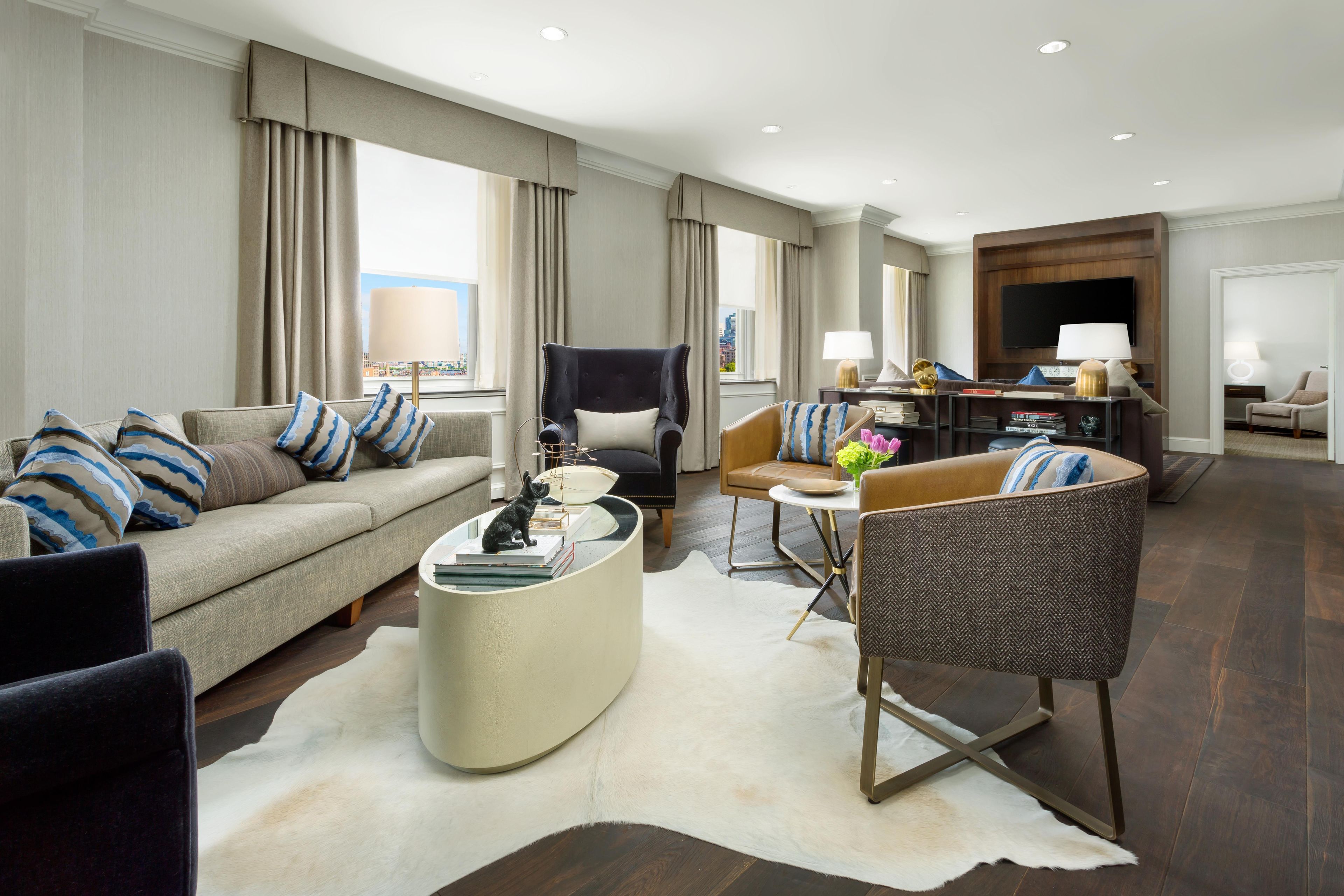 A modern hotel living room with a sofa, armchairs, a coffee table, and a TV.