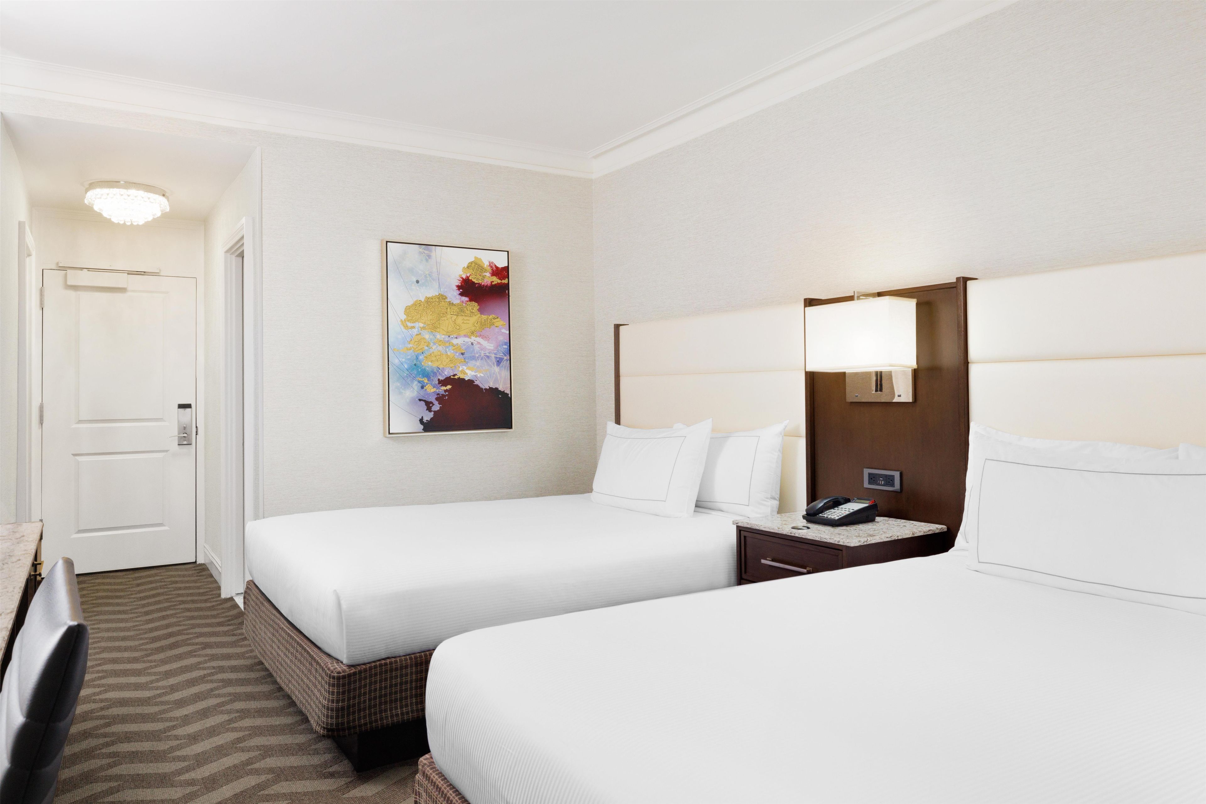 A hotel room with two beds, a nightstand with a phone, and a painting on the wall.