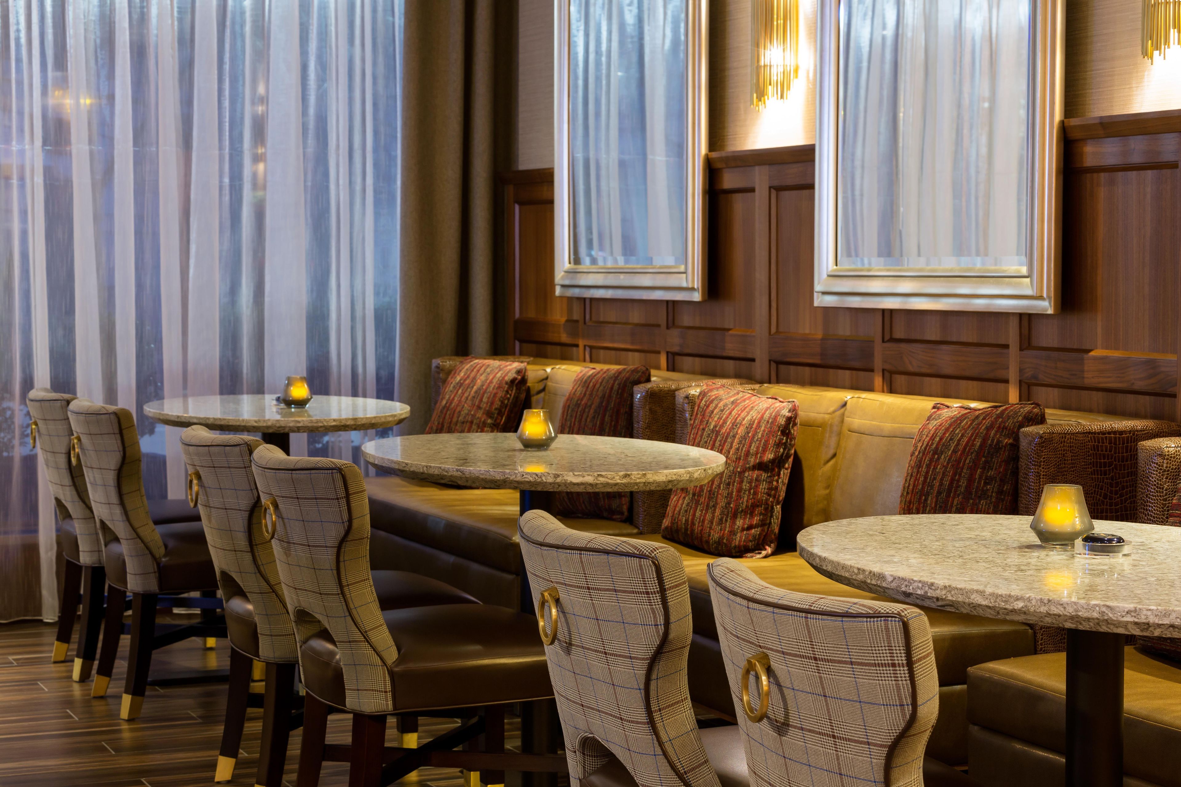 A restaurant with round tables and cushioned seating, featuring a warm ambiance and wooden paneling.