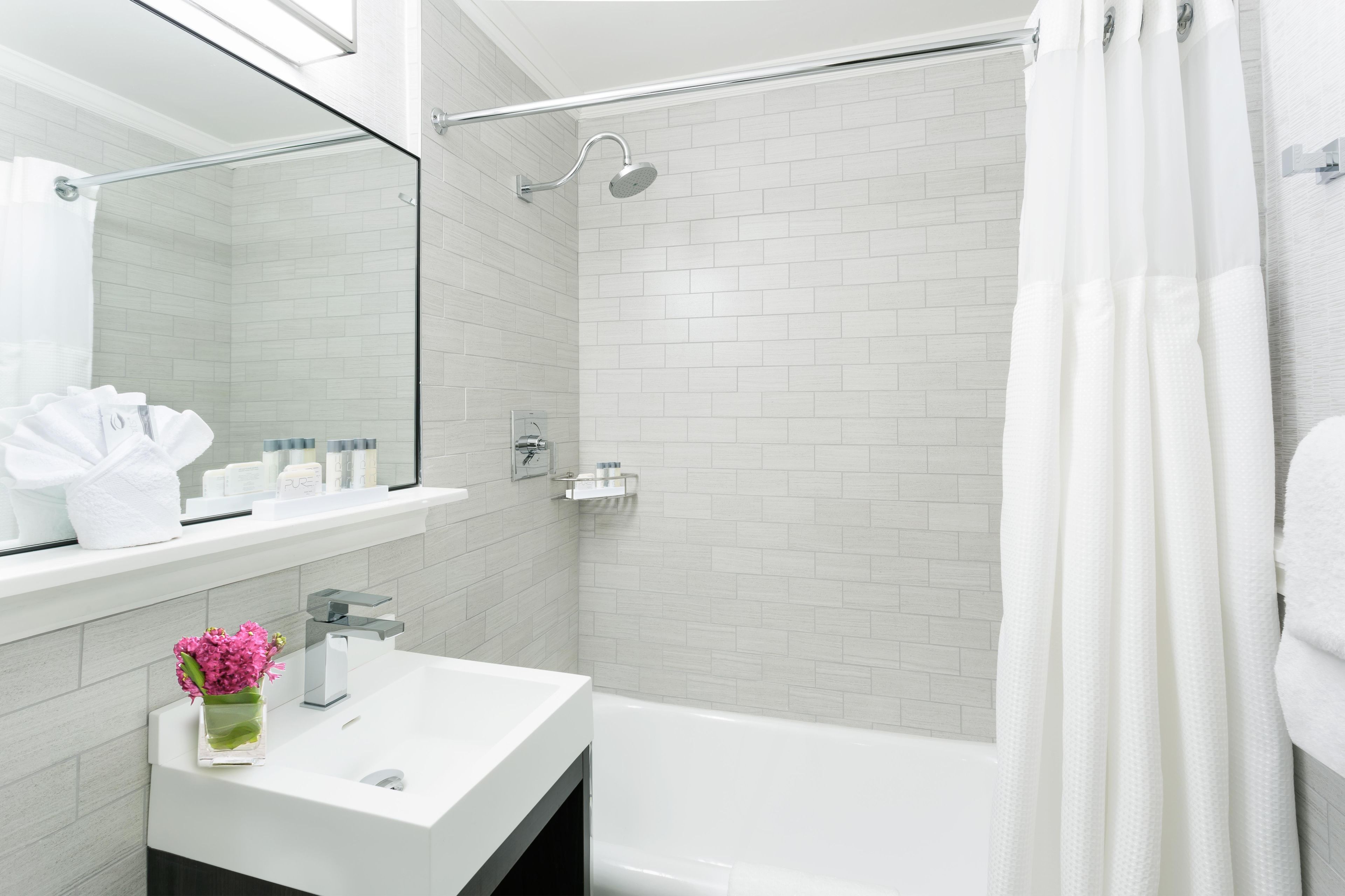 A modern bathroom with a white sink, mirror, and shower area.