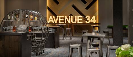 Et barområde med et skilt der viser 'AVENUE 34' og en bardisk med glas og flasker.