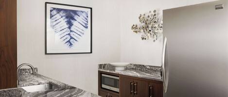 A modern kitchen with a granite countertop, stainless steel sink, microwave, and a refrigerator.