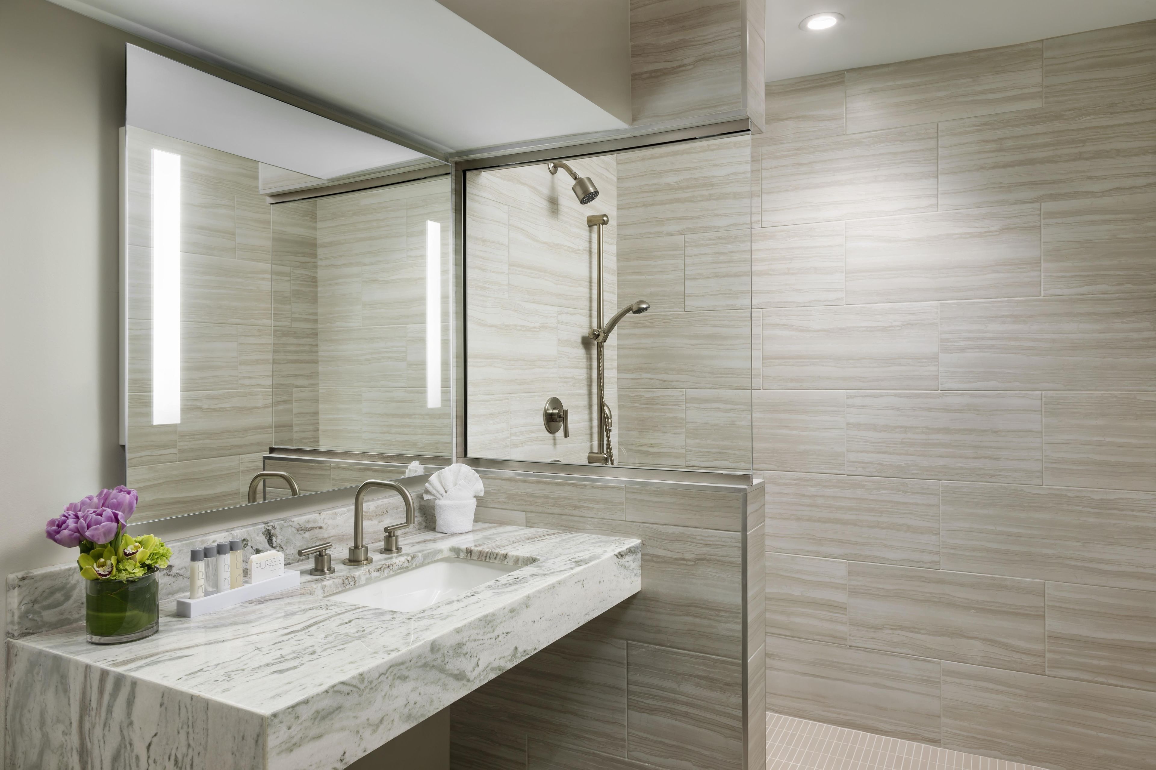 A modern bathroom with a marble sink, a glass-enclosed shower, and a large mirror.