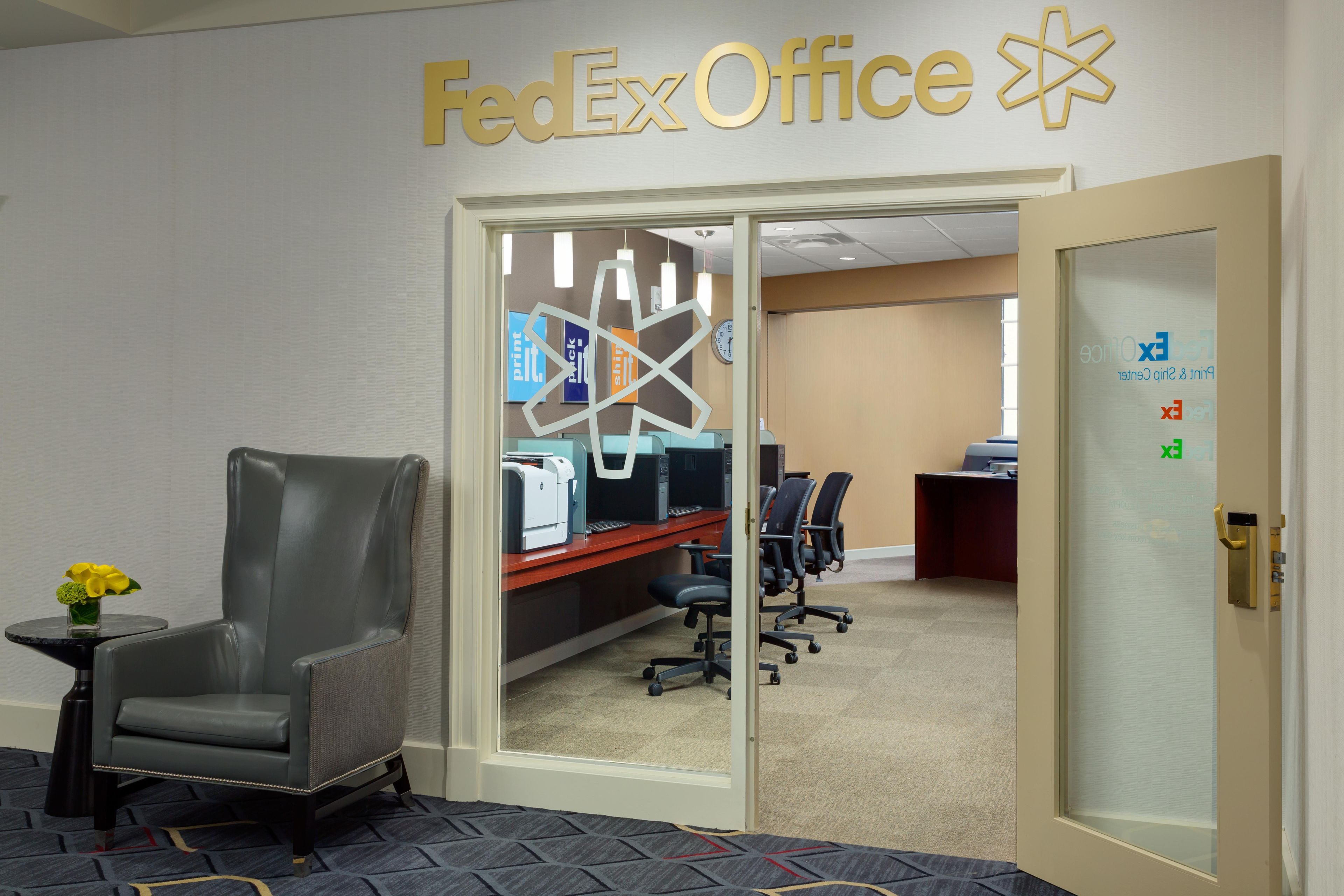 A FedEx Office workspace with office chairs, computers, and a clock on the wall.