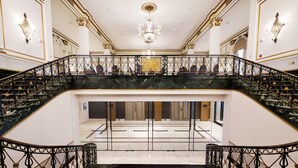 Eine prächtige Treppe mit Marmorstufen und aufwendigen schwarzen Geländern, die zu einer oberen Etage mit einem Kronleuchter führt.