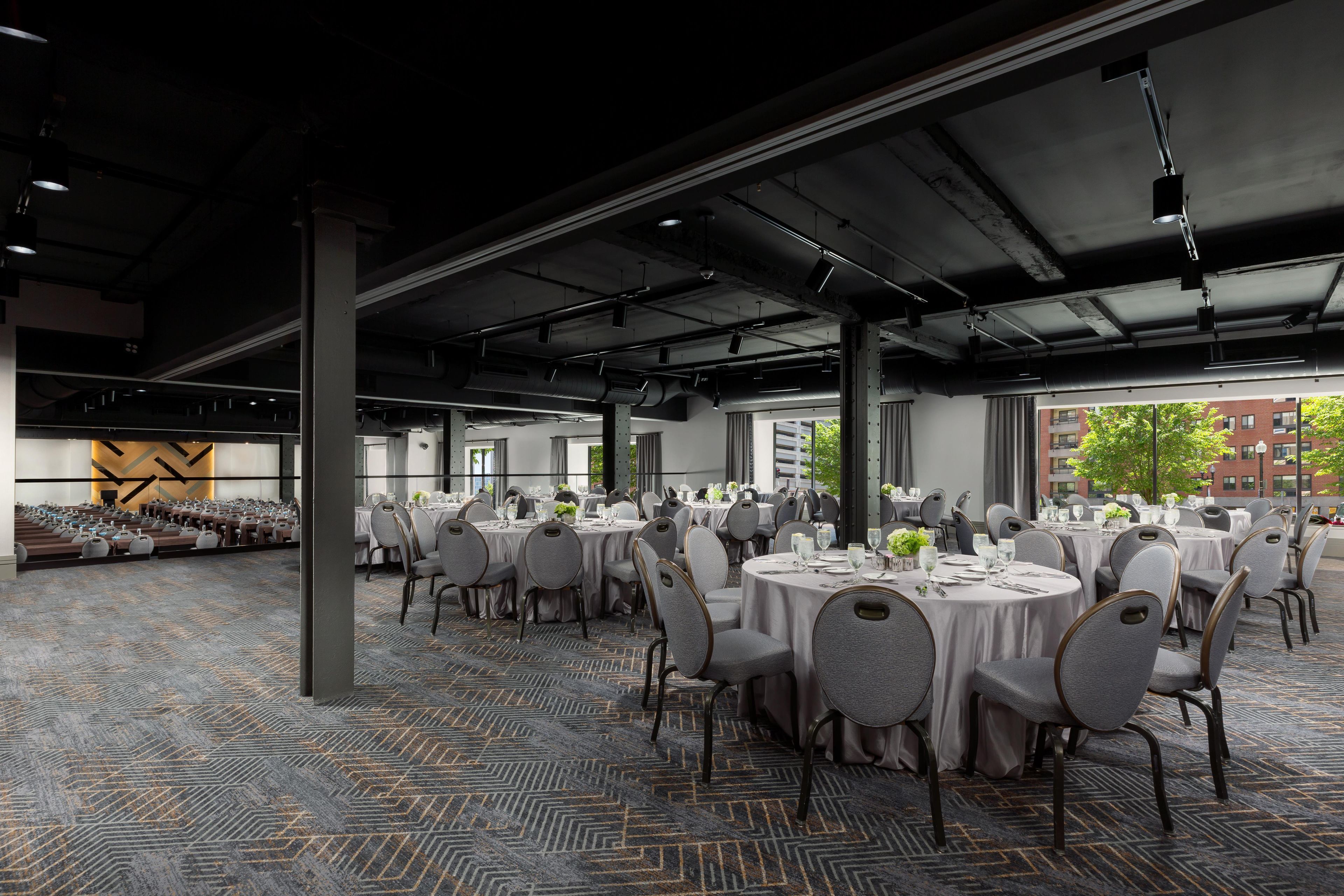 A spacious indoor dining area with round tables, grey upholstered chairs, and a patterned carpet.