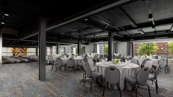 A spacious indoor dining area with round tables, grey upholstered chairs, and a patterned carpet.
