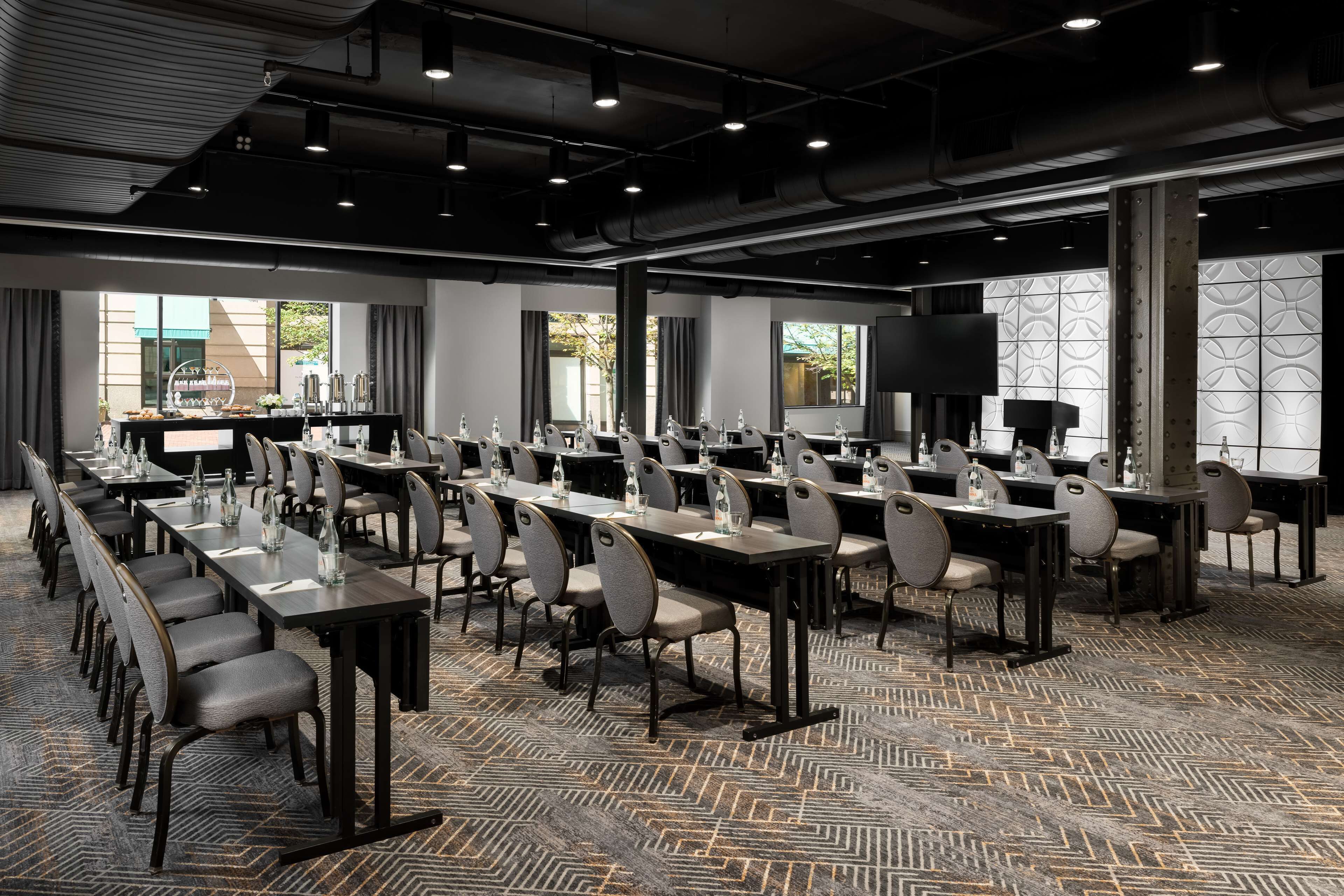 A conference room with long tables, chairs, and a large screen.