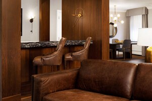 Une chambre d’hôtel moderne avec un canapé en cuir, un comptoir en marbre et un coin repas agrémenté d’un lustre.